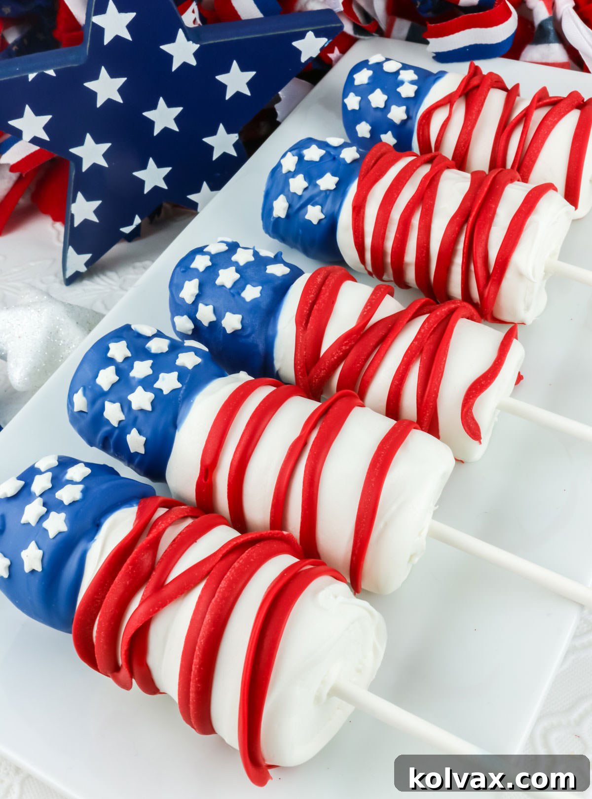 Red White and Blue Marshmallow Pops 6 Five red white and blue American Flag Marshmallow Pops laying on a white serving platter on a white table in front of 4th of July decorations. A delightful and easy 4th of July dessert.