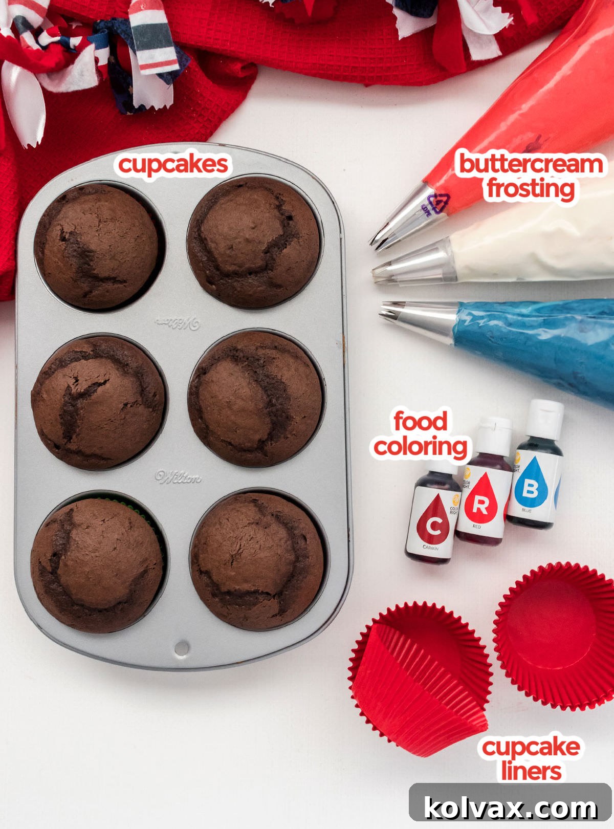 A comprehensive flat lay of all necessary ingredients to bake Patriotic Swirl Cupcakes, including baked chocolate cupcakes, tubs of buttercream frosting, bottles of blue and red food coloring, and a stack of vibrant red cupcake liners.
