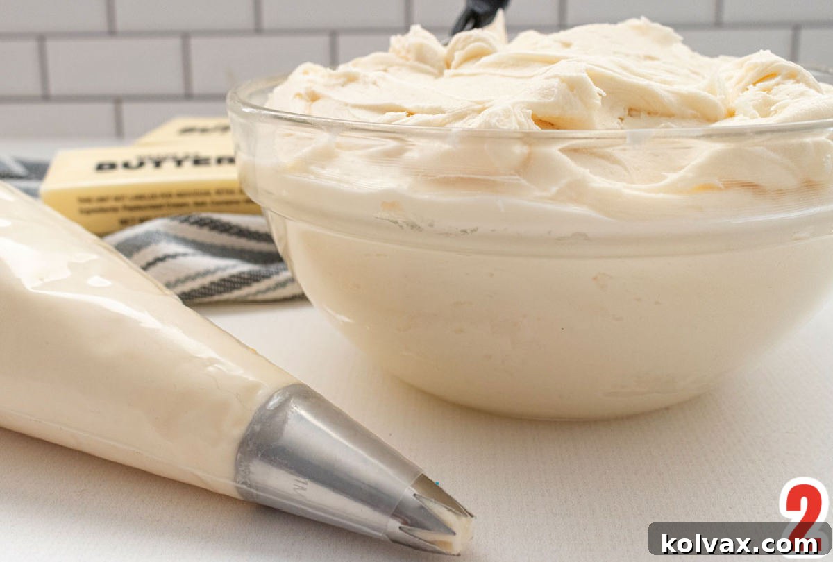 A pristine glass bowl filled with freshly made homemade Buttercream Frosting sits beside a professional decorating bag, also brimming with the creamy frosting, indicating readiness for application.
