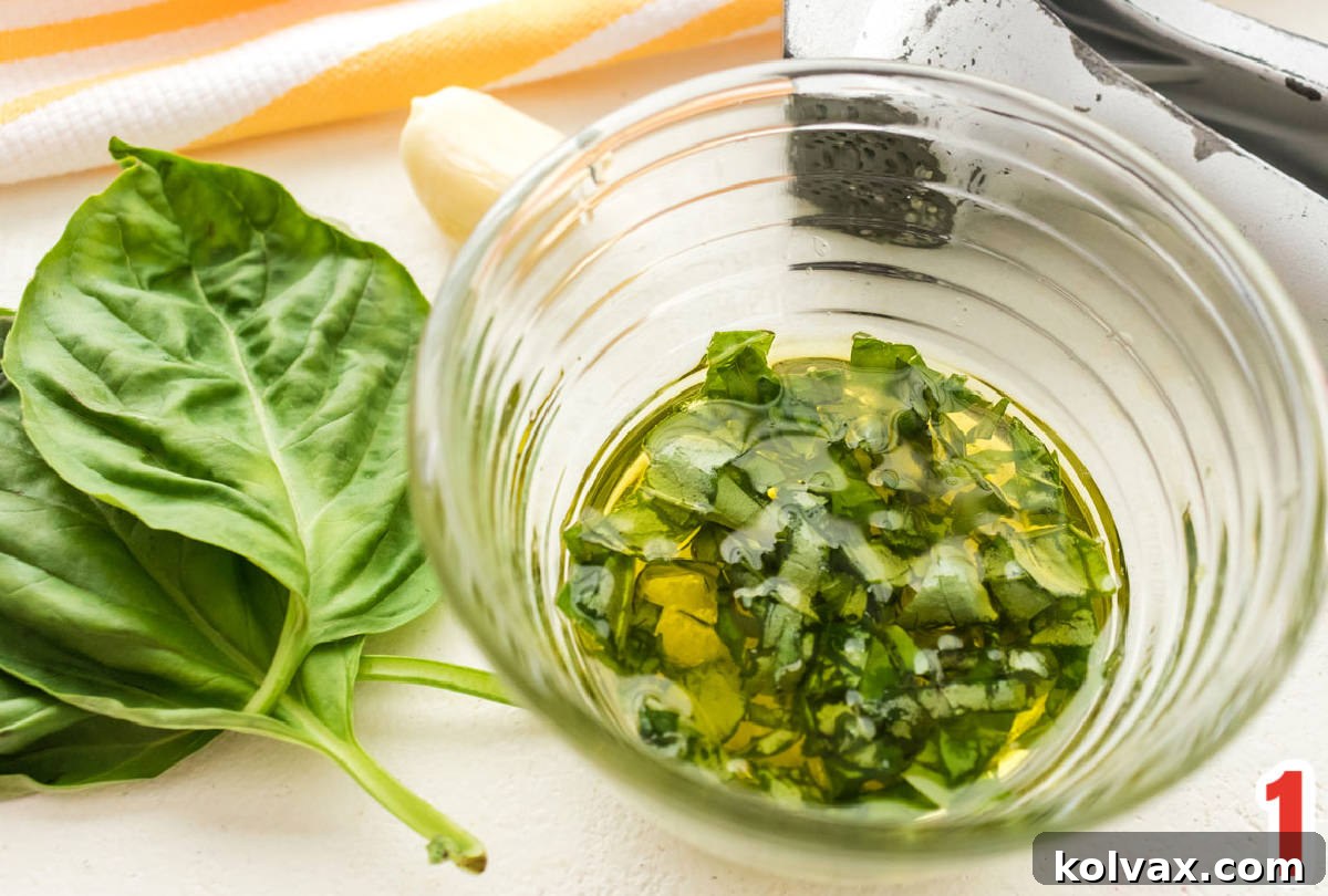 Closeup on a bowl of Garlic Basic Salad Dressing next to fresh basil leaves and a garlic press.