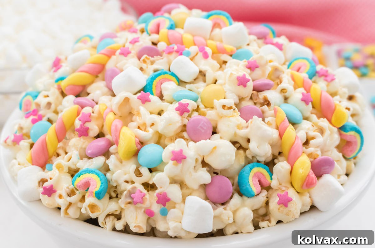 Closeup on a white serving bowl filled with Unicorn Popcorn with a ramekin of M&M's and a bowl of marshmallows in the background.