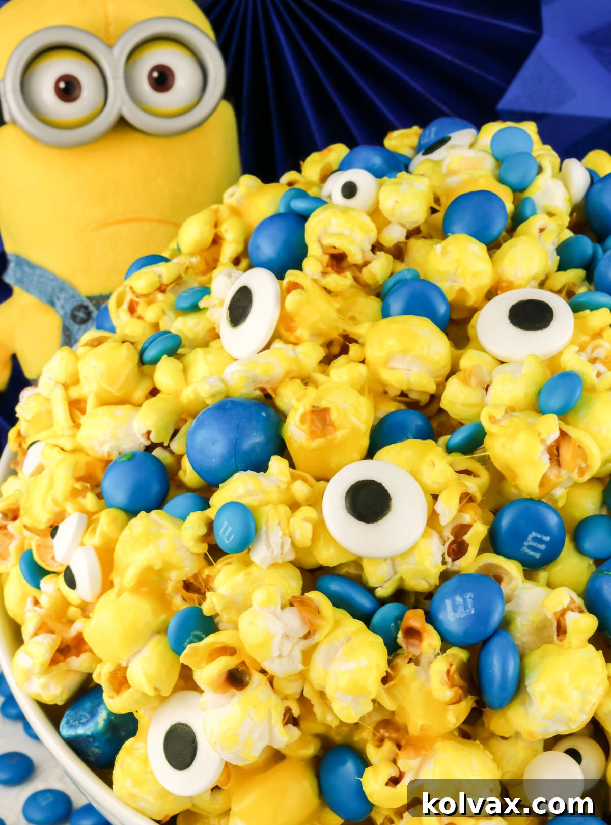 Closeup of Minions Popcorn in a white serving bowl sitting next to a Minions Plushie in front of a blue background.
