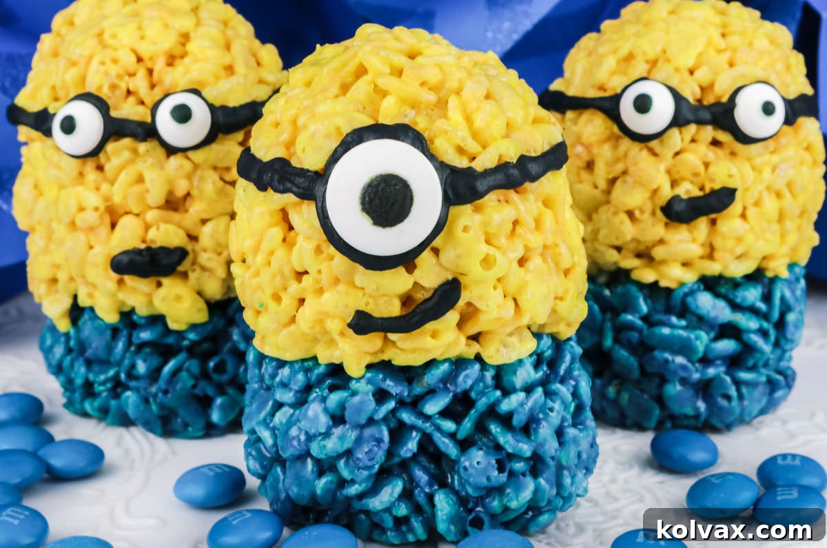 Three Minions Rice Krispie Treats on a white surface with blue M&Ms, ready for a Minion-themed party.
