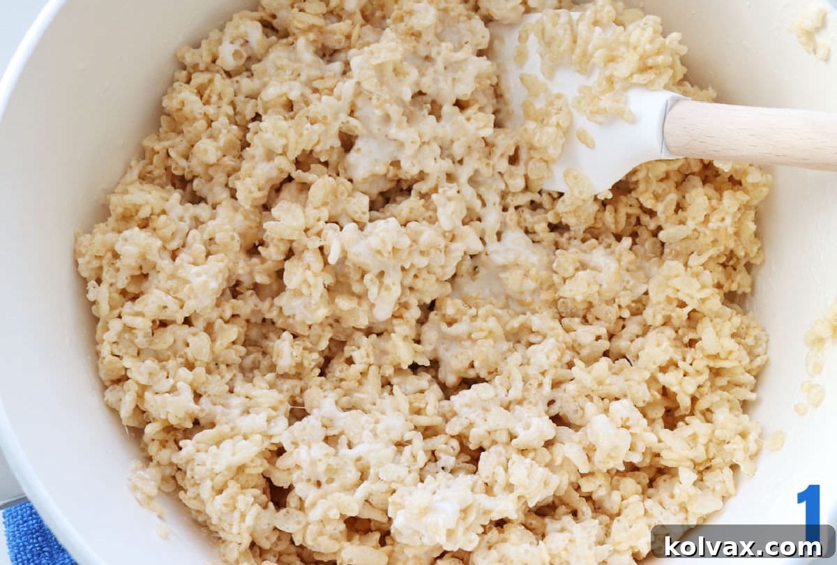 Rice Krispie Treat mixture in a white pan, stirred with a white wooden spatula.