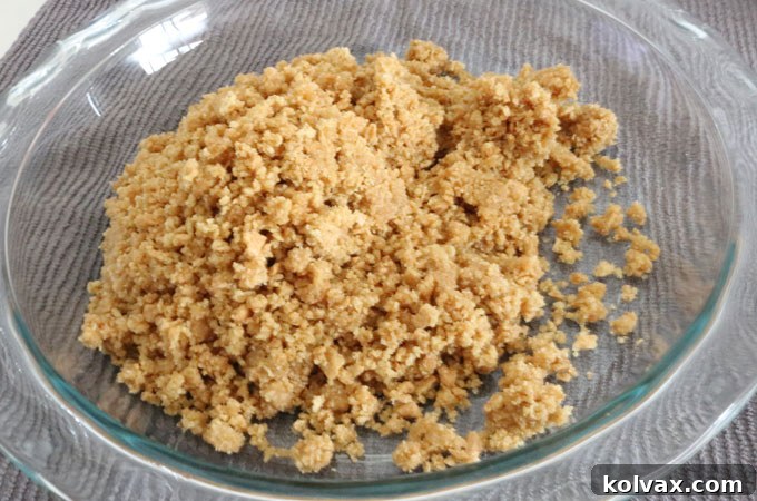 The butter-coated graham cracker crumbs being poured from the plastic bag into a 9-inch glass pie plate.