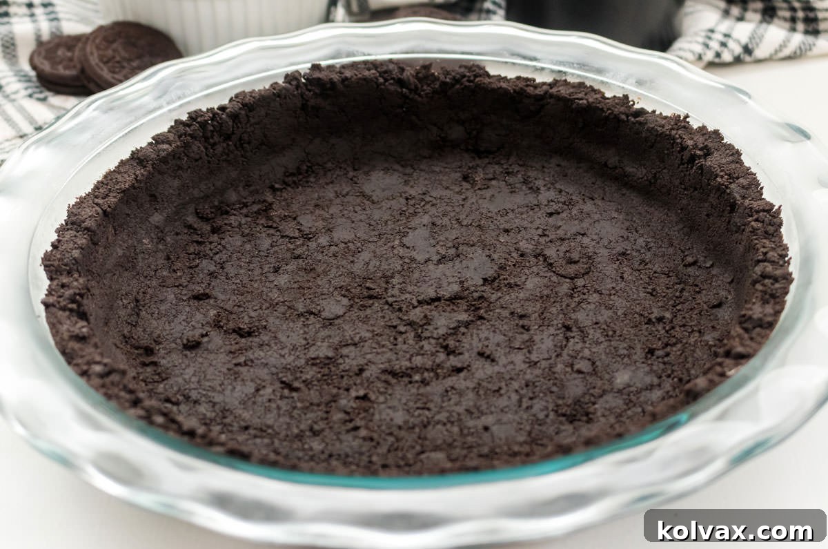 A perfectly formed Oreo Cookie Pie Crust in a clear glass pie plate, ready for filling, sitting on a pristine white surface.