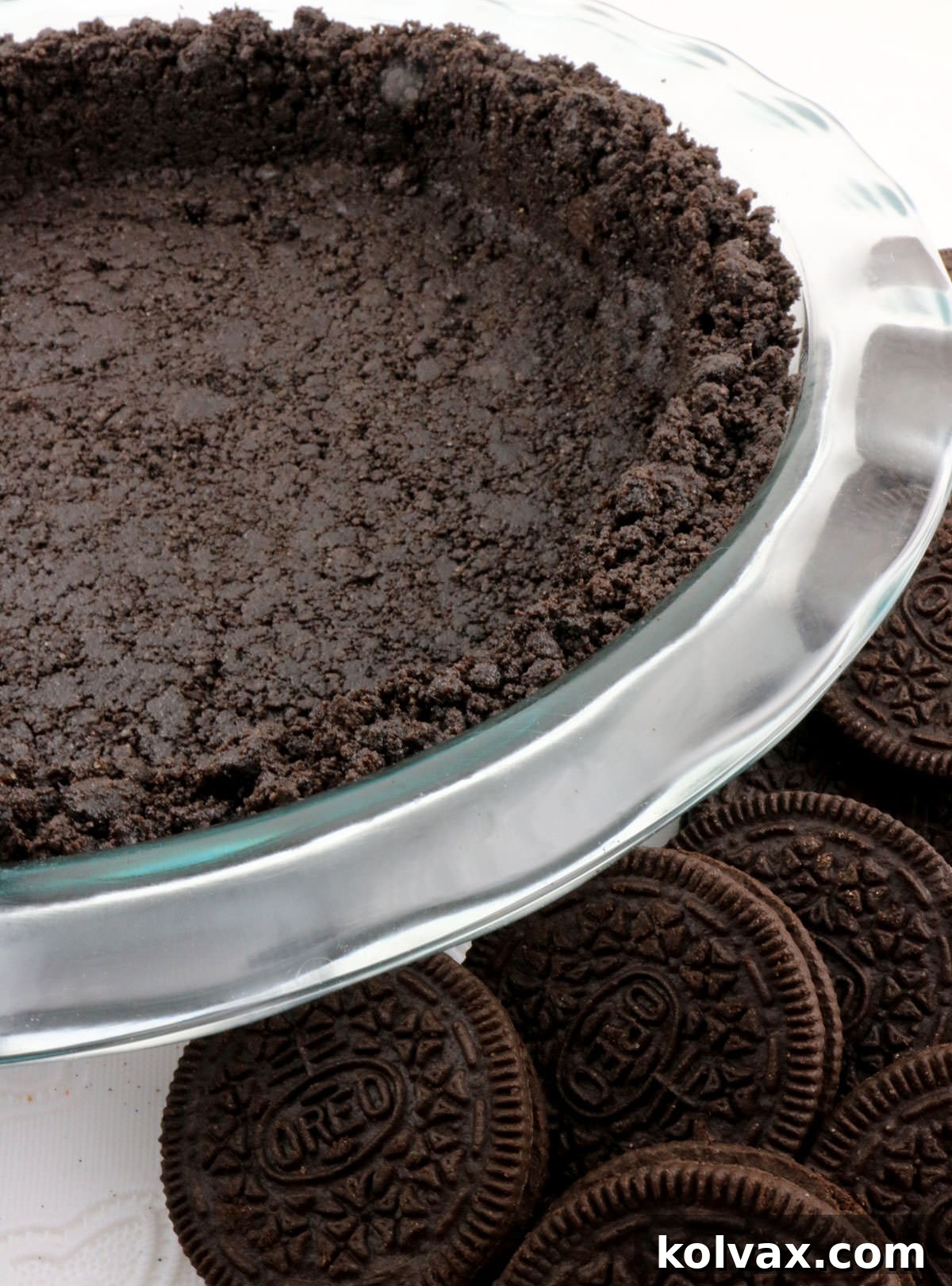 A stunning close-up of a finished Oreo cookie pie crust, nestled in a glass pie pan, surrounded by whole Oreo cookies, emphasizing its rich texture and readiness for filling.