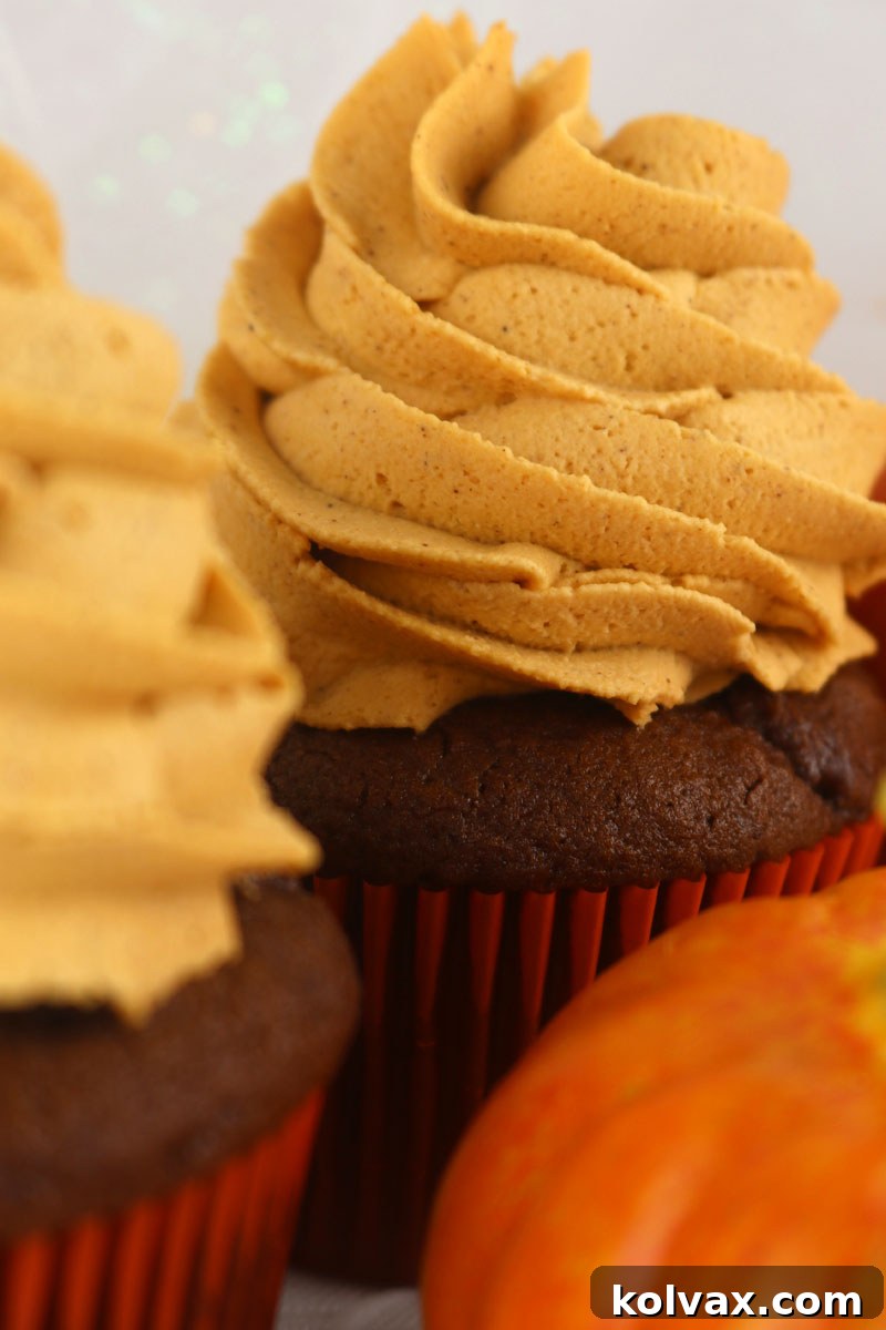 A close-up of a cupcake adorned with a perfect, stable swirl of Pumpkin Spice Whipped Cream Frosting, showcasing its smooth texture and readiness to be devoured.