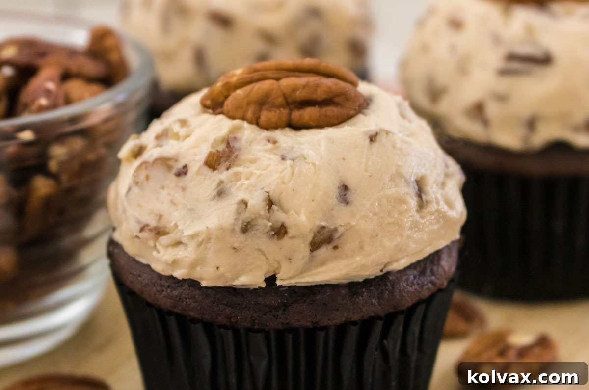 Closeup on a cupcake topped with Maple Pecan Buttercream Frosting sitting next to a glass bowl filled with pecans.