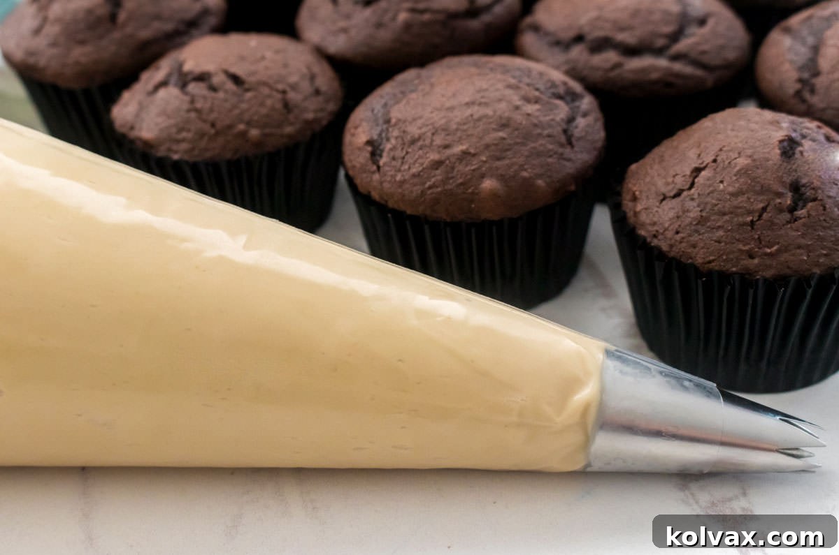Heavenly Brown Sugar Cream Cheese Frosting 5 Close-up of a pastry bag expertly filled with the rich Brown Sugar Cream Cheese Frosting, positioned in front of a tray of unfrosted chocolate cupcakes, ready for decoration.