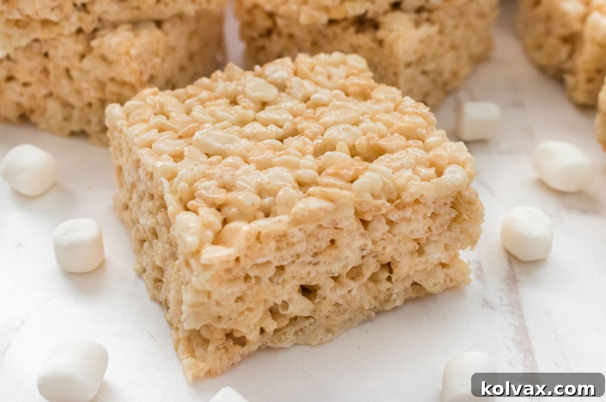 Closeup shot of our The Best Ever Rice Krispie Treat sitting on a white table surrounded by Mini Marshmallows.