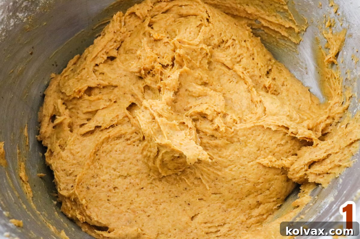 Metal mixing bowl filled with rich, orange Pumpkin Cake Batter, ready for baking.