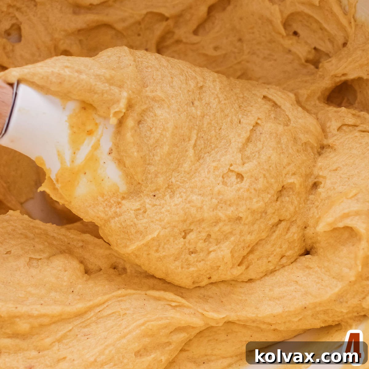 Closeup on a white bowl filled with creamy Pumpkin Spice Buttercream Frosting and a white spatula, highlighting its rich texture and color.