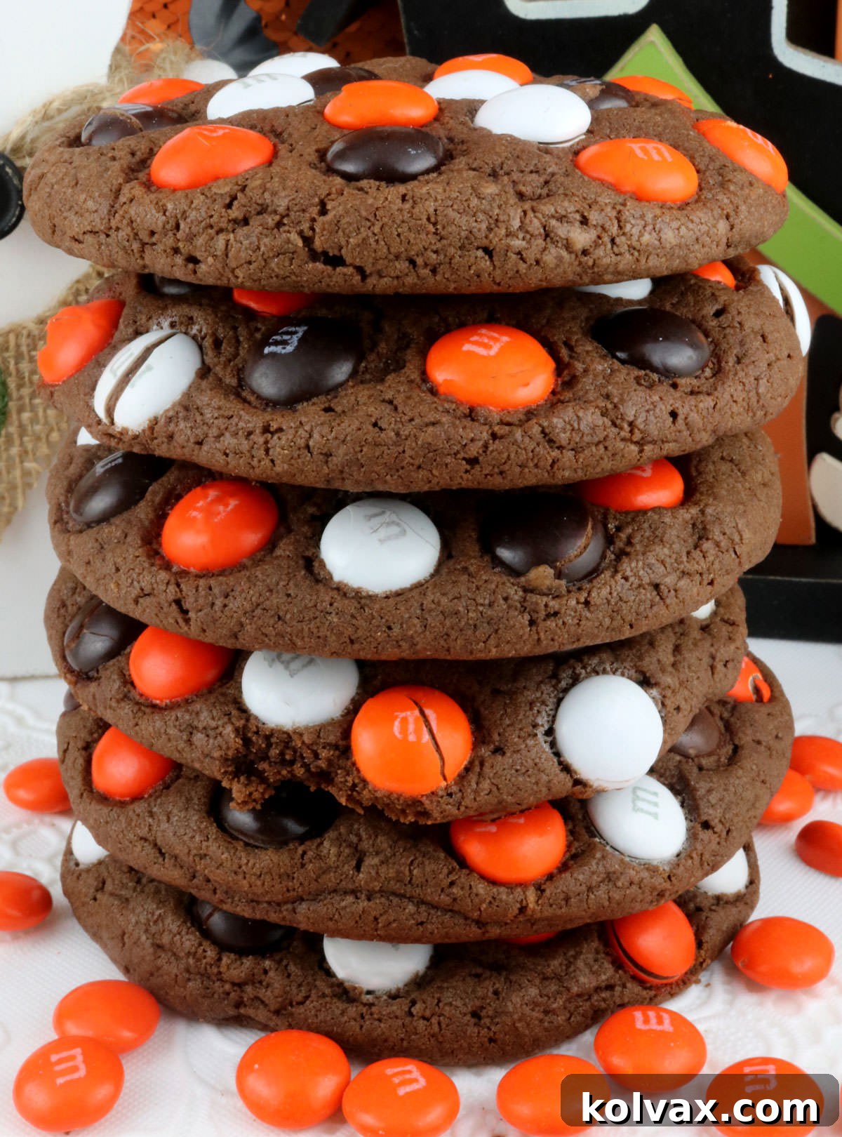 Closeup on a stack of delicious Halloween M&M Cookies sitting on a pristine white table, surrounded by scattered orange M&M's.