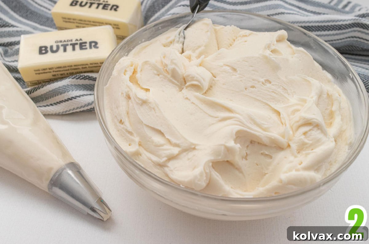Clear glass bowl filled with buttercream frosting sitting next to butter, a decorating bag filled with frosting and a black and white towel.