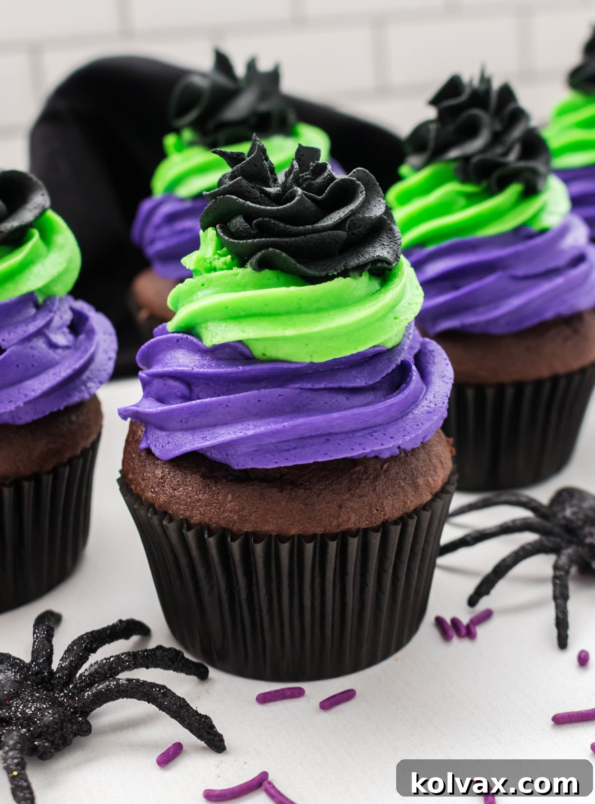 Closeup on five Bewitched Halloween Cupcakes sitting on a white table surround by toy spiders and sprinkles.