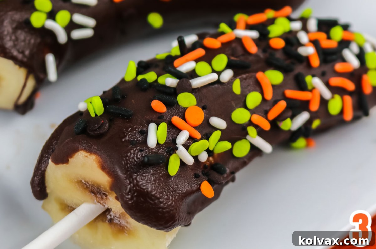 Close-up of a single homemade Halloween frozen banana generously coated in chocolate and topped with vibrant Halloween sprinkles.