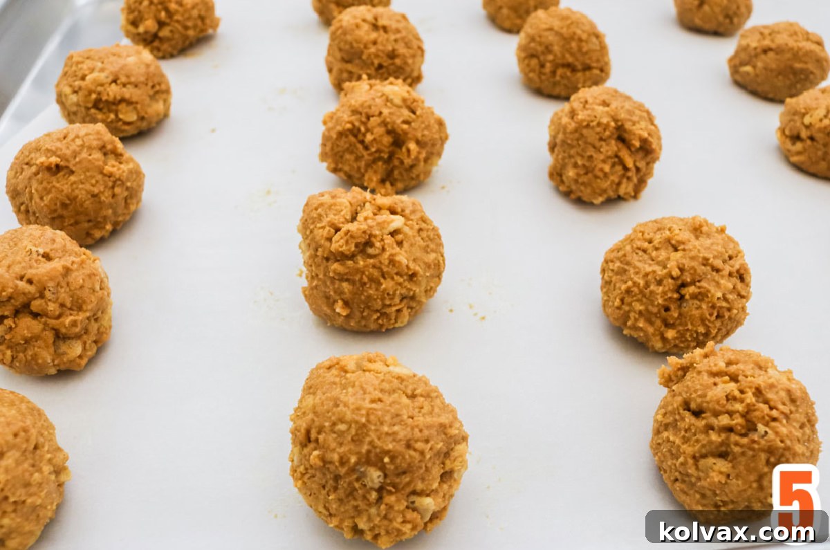 Perfectly formed Peanut Butter Crunch Balls neatly arranged on a parchment-lined cookie sheet, ready for their final chilling before chocolate coating.