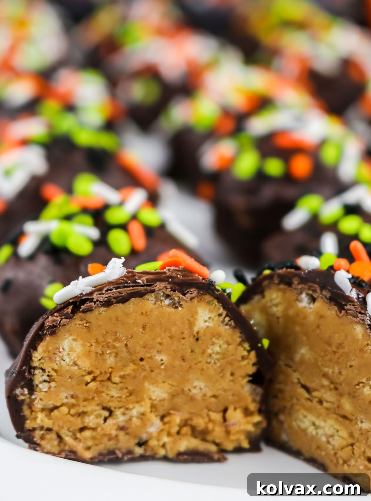 A close-up of beautifully finished Peanut Butter Crunch Balls on a white serving platter, with one cut in half to clearly reveal its creamy, crunchy interior layers.