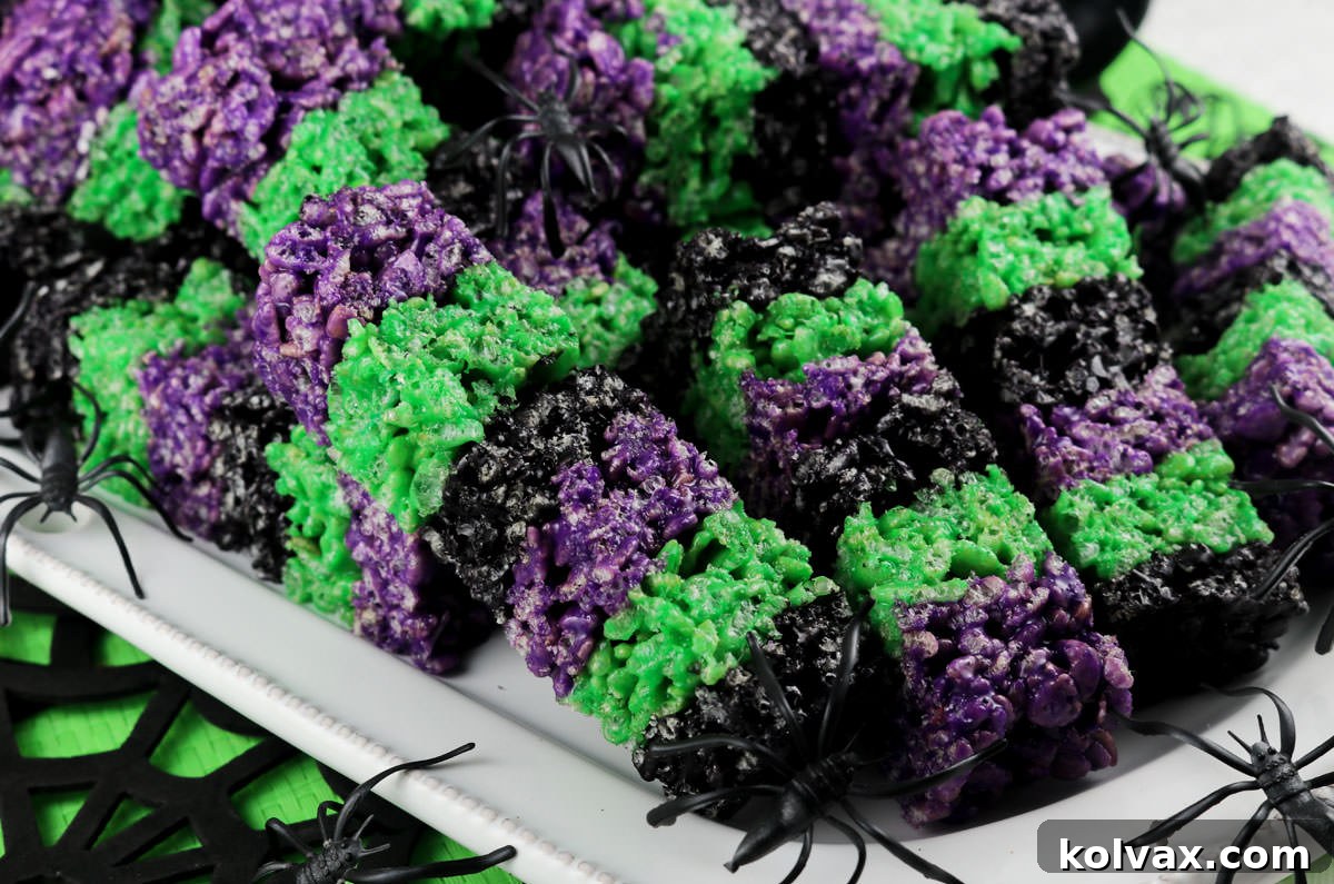 Closeup on a stack of Bewitched Rice Krispie Treat Wands sitting on a white serving platter surrounded by toy spiders and Halloween decorations. The wands are purple, green, and black, making them perfectly spooky.
