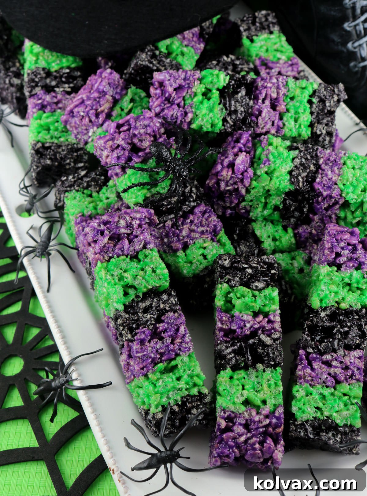 Closeup on a plate of vibrantly colored Bewitched Rice Krispie Treat Wands sitting on a table decorated for Halloween, ready to be enjoyed.