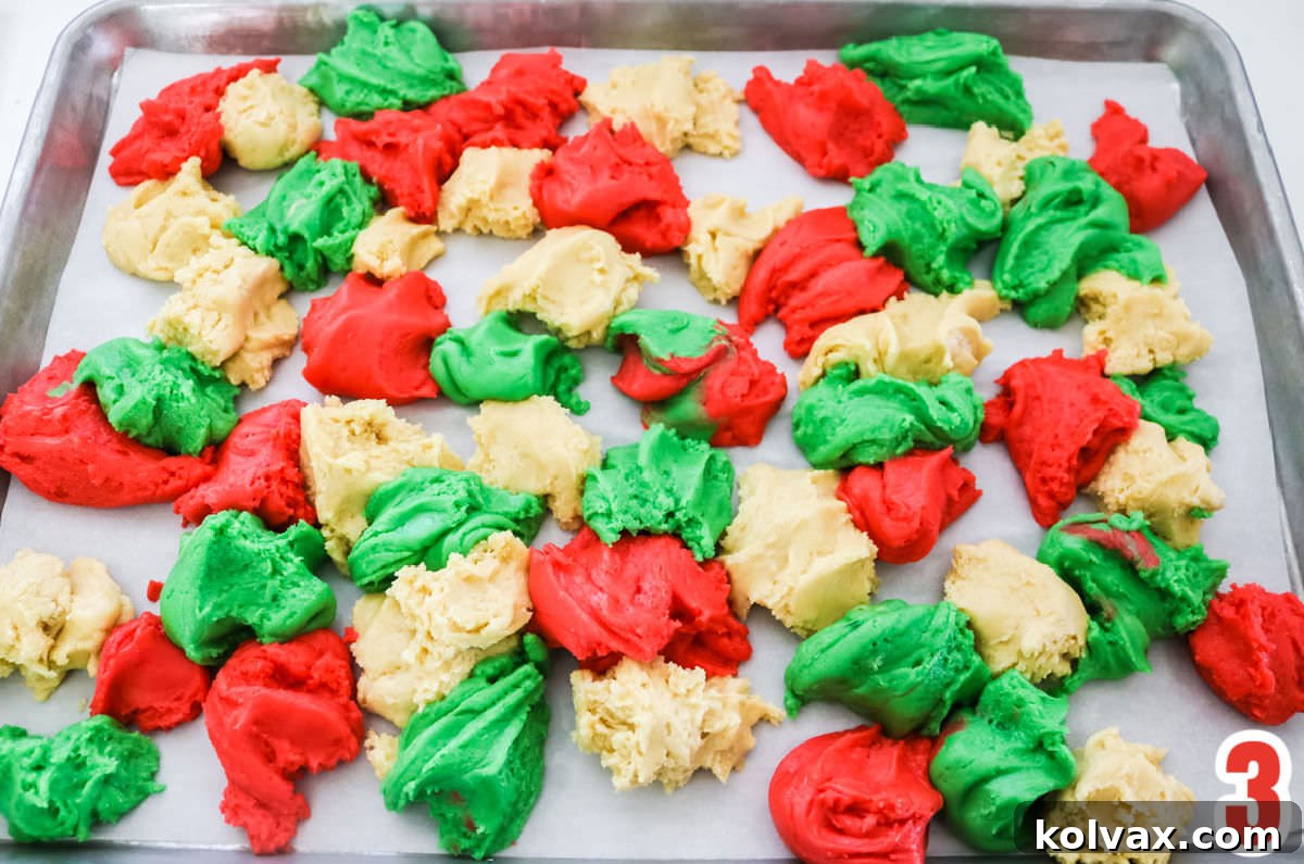 Overhead shot of a cookie sheet lined with parchment paper, artfully arranged with random pieces of green, red, and white sugar cookie bar dough, creating a beautiful marble pattern before baking.