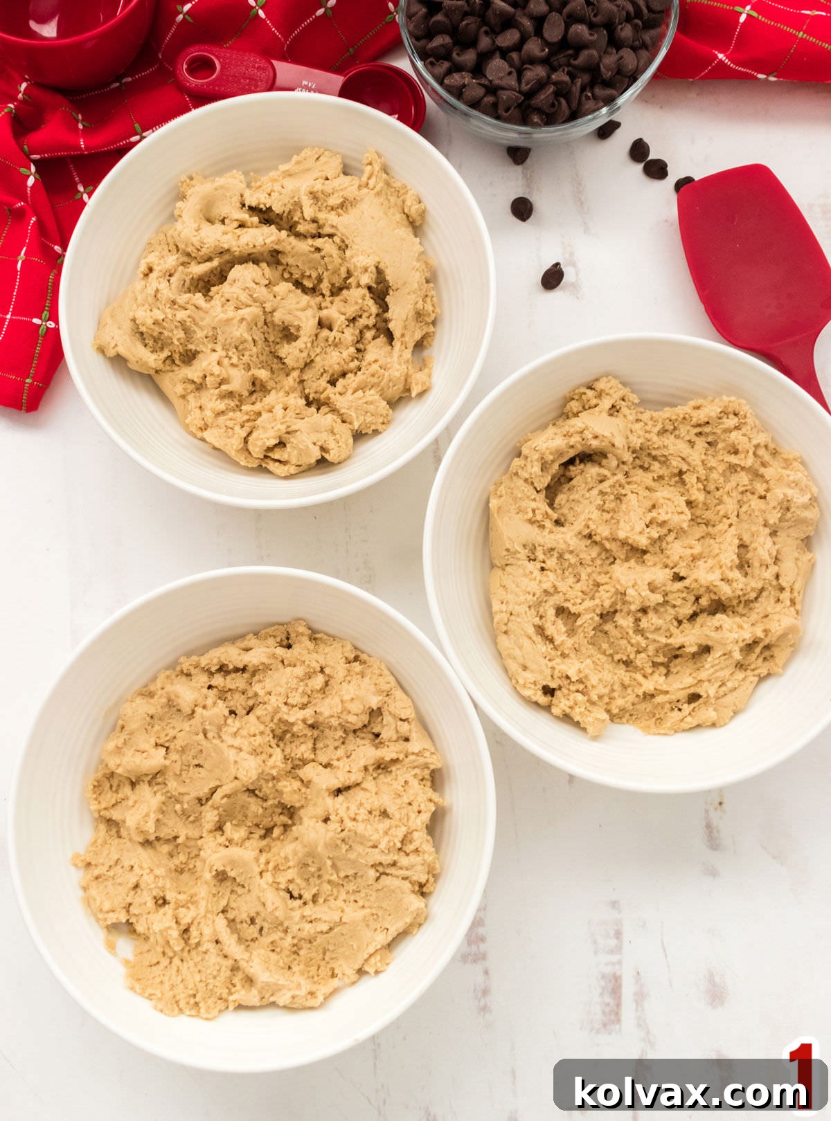 Closeup on three white bowls sitting on a white table filled with cookie dough.