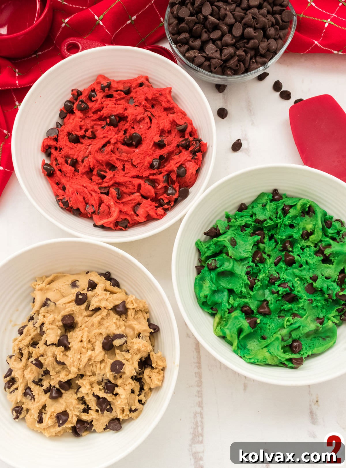 Three bowls sitting on a white table filled with regular Chocolate Chip Cookie dough and red and green Chocolate Chip Cookie Dough.