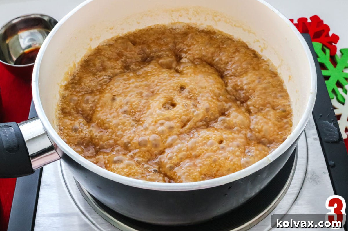 Close-up of a bubbling caramel mixture in a saucepan on a stovetop, showing the cooking process.