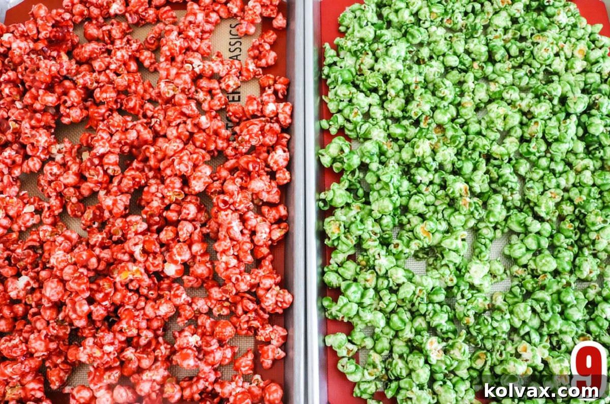 Overhead view of two cookie sheets, one filled with vibrant red caramel corn and the other with festive green caramel corn, cooling.