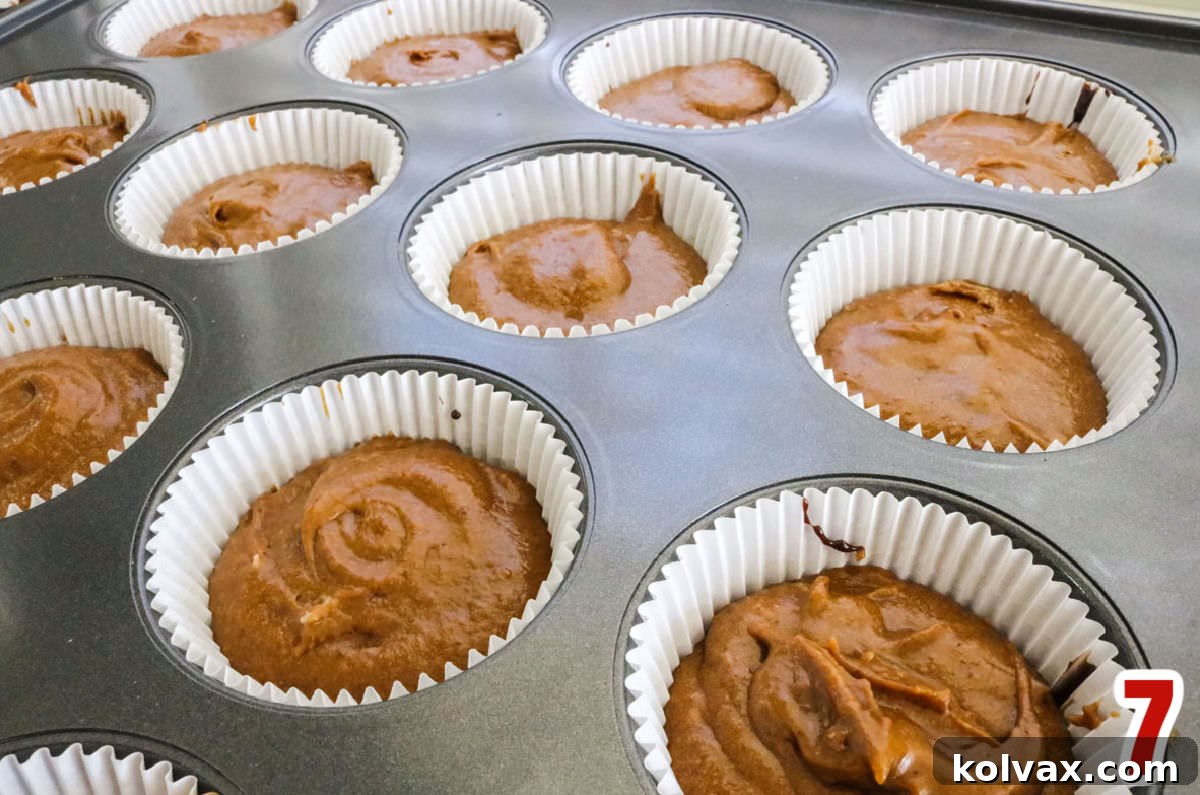 A cupcake baking pan filled with cupcake liners, each containing a base of brownie batter topped with a generous layer of spiced gingerbread cake batter, ready for baking.