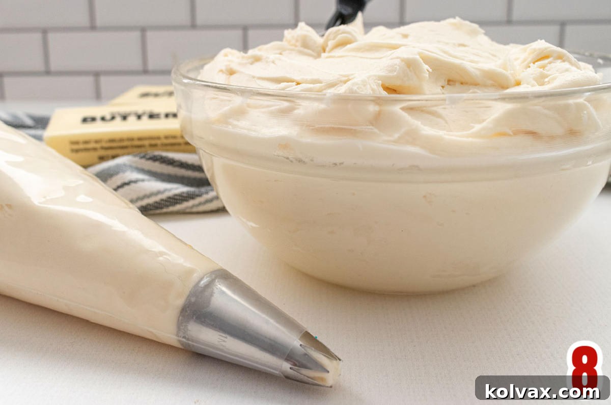 A glass bowl overflowing with smooth, creamy white buttercream frosting sits beside a piping bag filled with the same frosting, ready for decorating festive cupcakes.