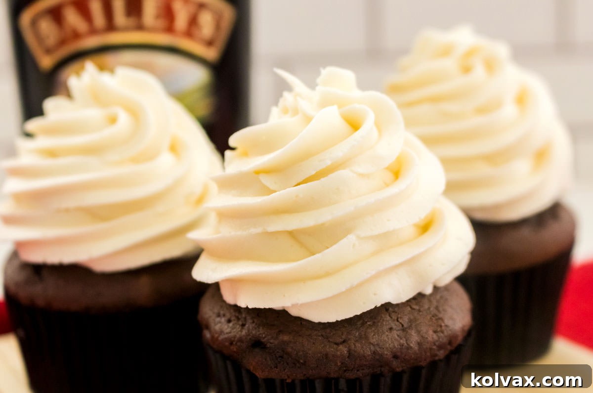 Three decadent cupcakes frosted with creamy Baileys Irish Cream Buttercream, artfully arranged on a wooden board next to a bottle of Baileys Irish Cream Liqueur.