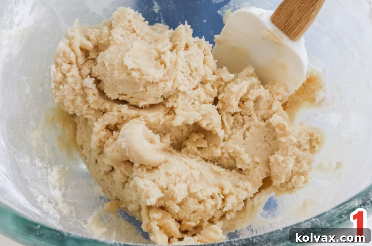 Clear glass mixing bowl filled with Cookie dough and a white wooden spatula.