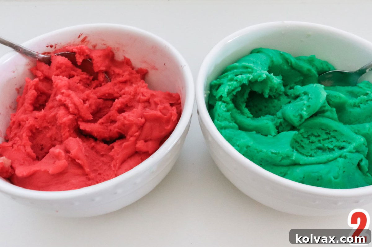 Two white bowls sitting on a white countertop. One filled with red cookie dough, the other with green cookie dough.