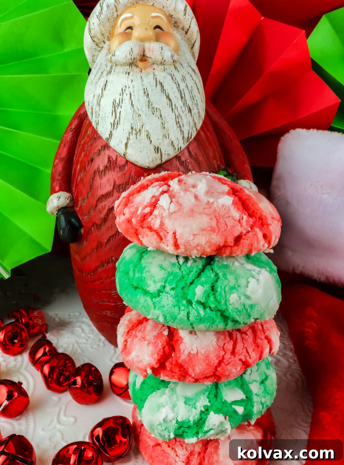 Stack of Red and Green Kris Kringle Crinkle Cookies sitting on a white table cloth in front of a Santa Claus Christmas decoration.