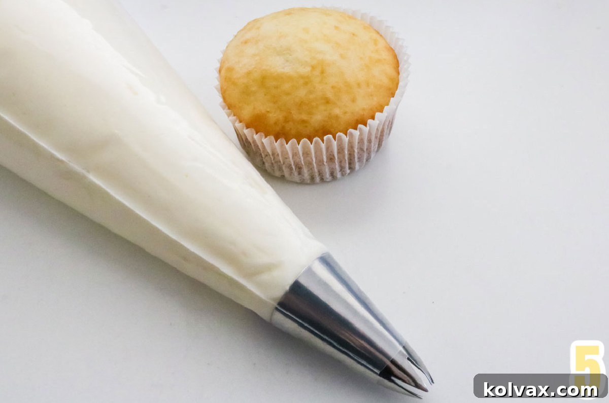 Overhead shot of a single white cupcakes and a decorating bag filled with homemade Champagne Buttercream Frosting.
