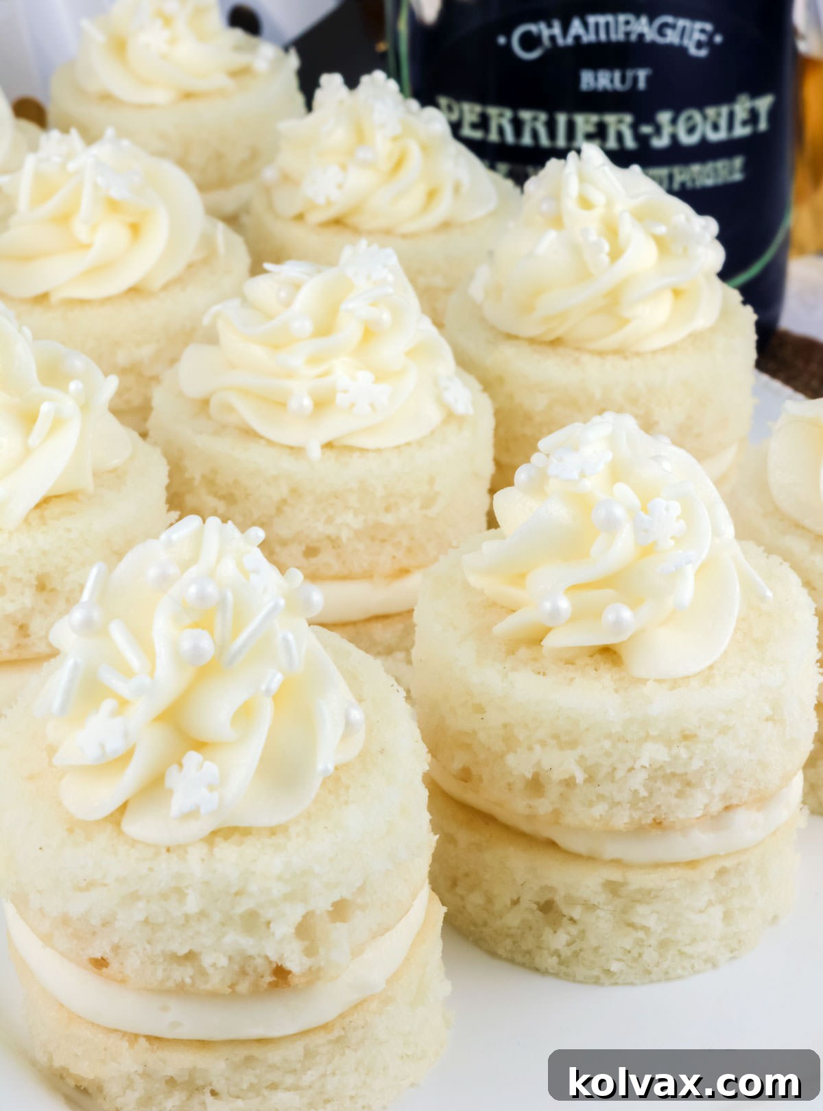 Closeup on a batch of Champagne Cake Bites sitting on a white serving platter next to a bottle of champagne.