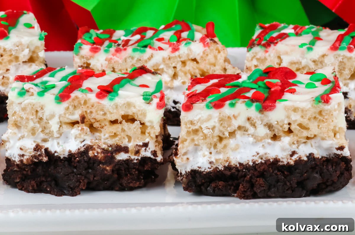 A close-up view of festive Christmas Brownie Rice Krispie Treats arranged on a white serving platter, adorned with red and green Christmas decorations in the background. Each bar reveals distinct layers of fudgy brownie, fluffy marshmallow, and crispy Rice Krispie treat.