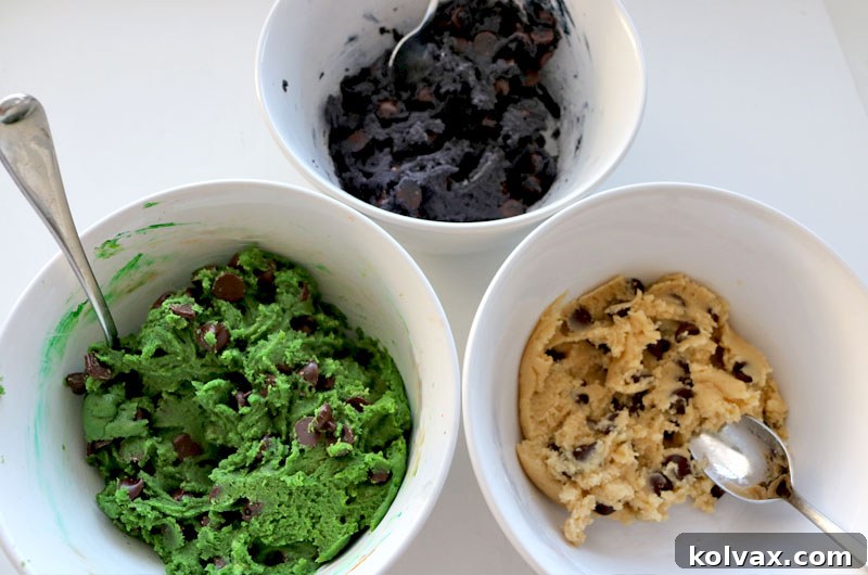 Three portions of cookie dough, two colored green and black, ready for chocolate chips.