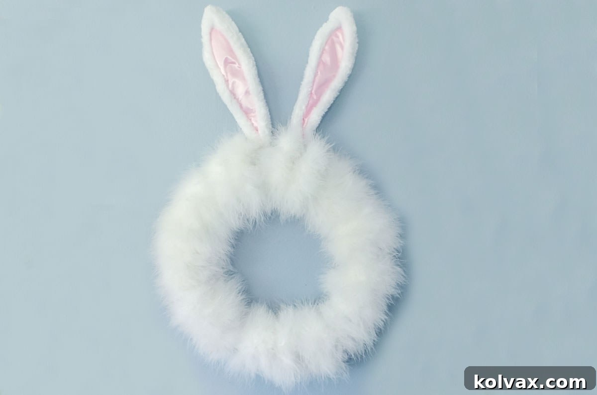 A beautifully crafted DIY Easter Bunny Wreath, featuring white feathers and bunny ears, hanging elegantly on a wall as a festive Easter decoration.