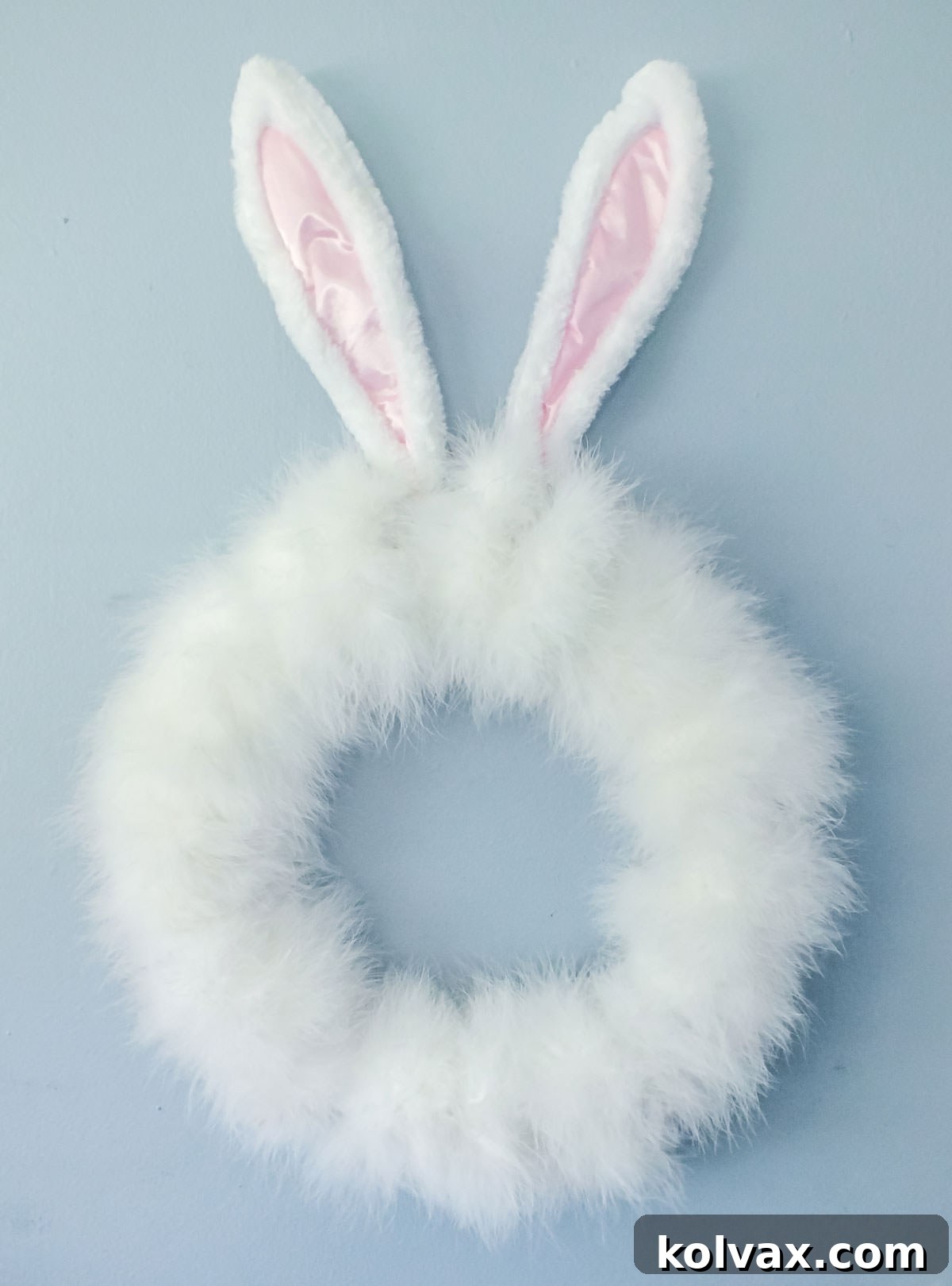 A delightful DIY Easter Bunny Wreath, adorned with soft white feathers and prominent bunny ears, hanging on a vibrant blue wall, ready to brighten any room.
