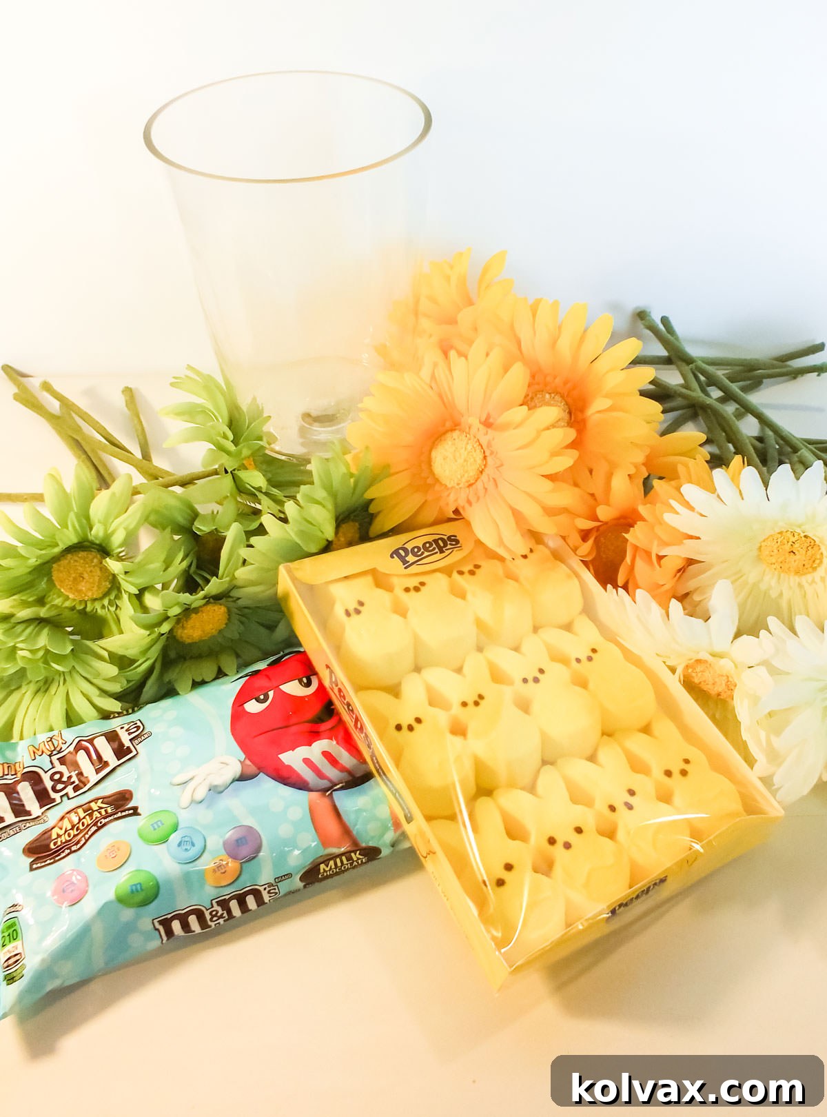 Supplies you will need to make an Easter Peeps Flower Arrangement including Easter M&M's, Peeps Bunny Candy, Artificial Flowers, Clear Glass Hurricane Vase, and skewers.