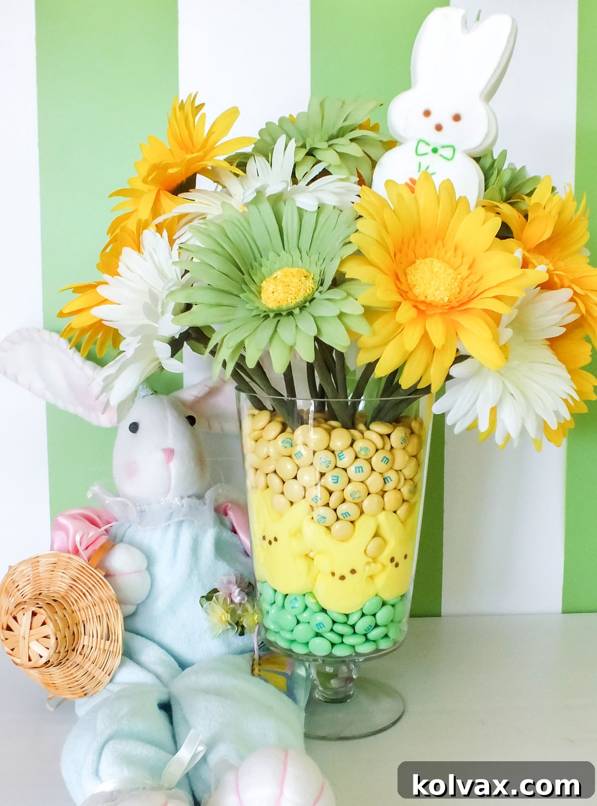 Closeup on a DIY Easter table Centerpiece featuring Peeps Candy, Easter M&M's and Artificial daisies, sitting elegantly on a white table.