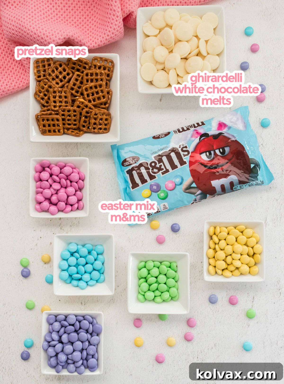 All the ingredients you will need to make Spring Flower Pretzel Bites including Easter Mix M&M's, Ghirardelli White Chocolate Melting Wafers and Hanover Pretzel Snaps laid out on a white surface.