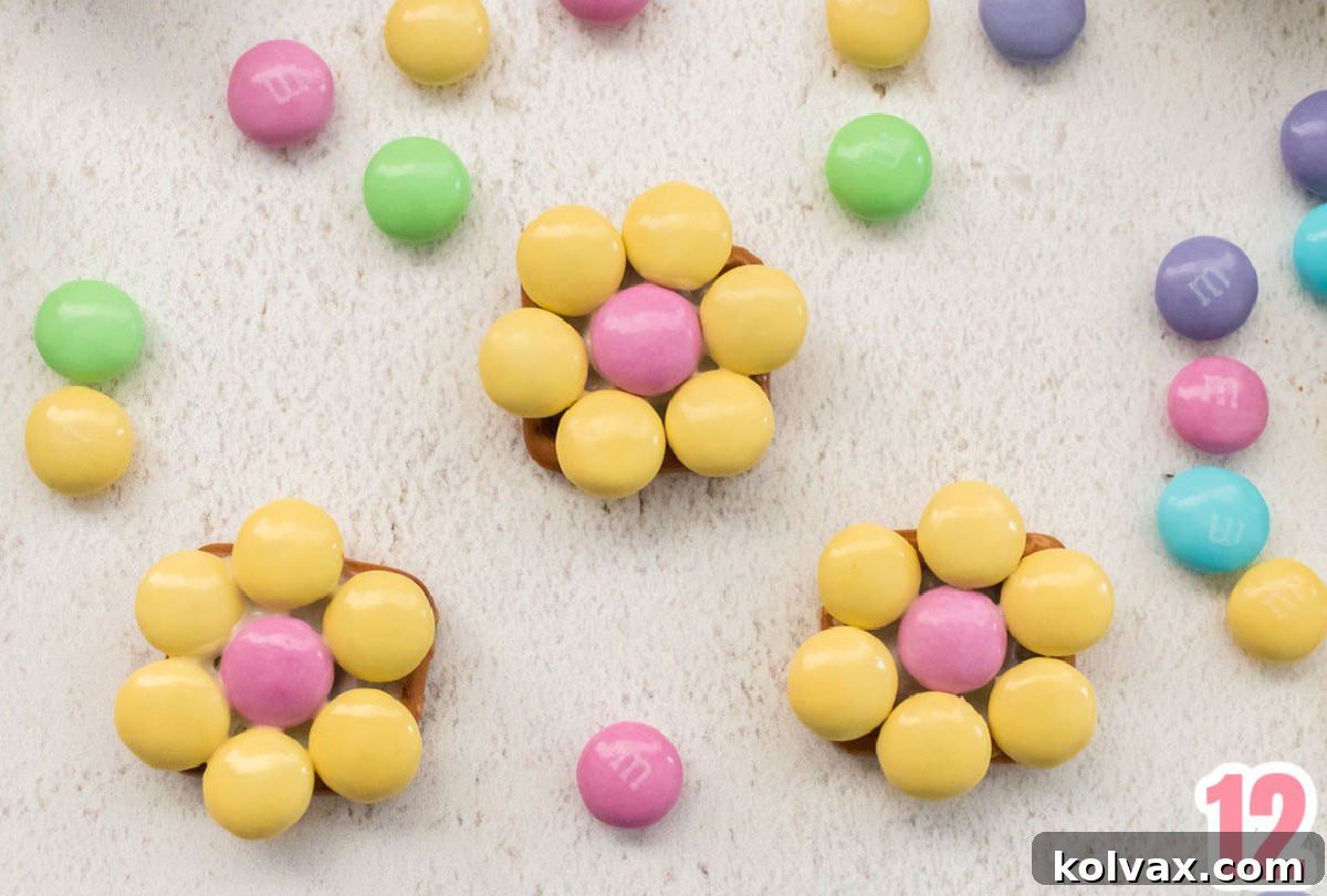 Close up on three finished Spring Flower Pretzel Bites laying on a white surface  surrounded by loose Easter M&M's.