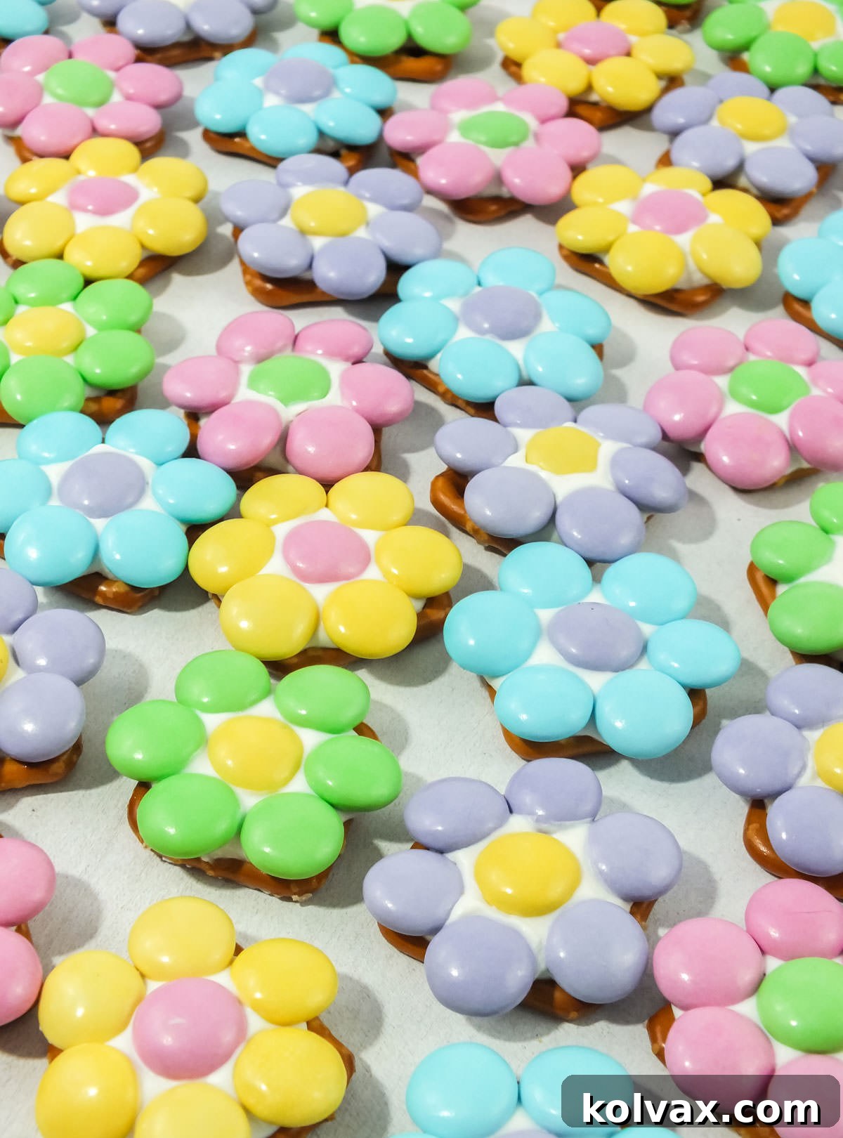 Closeup on many Spring Flower Pretzel Bites spread out across a white surface, showcasing various color combinations.