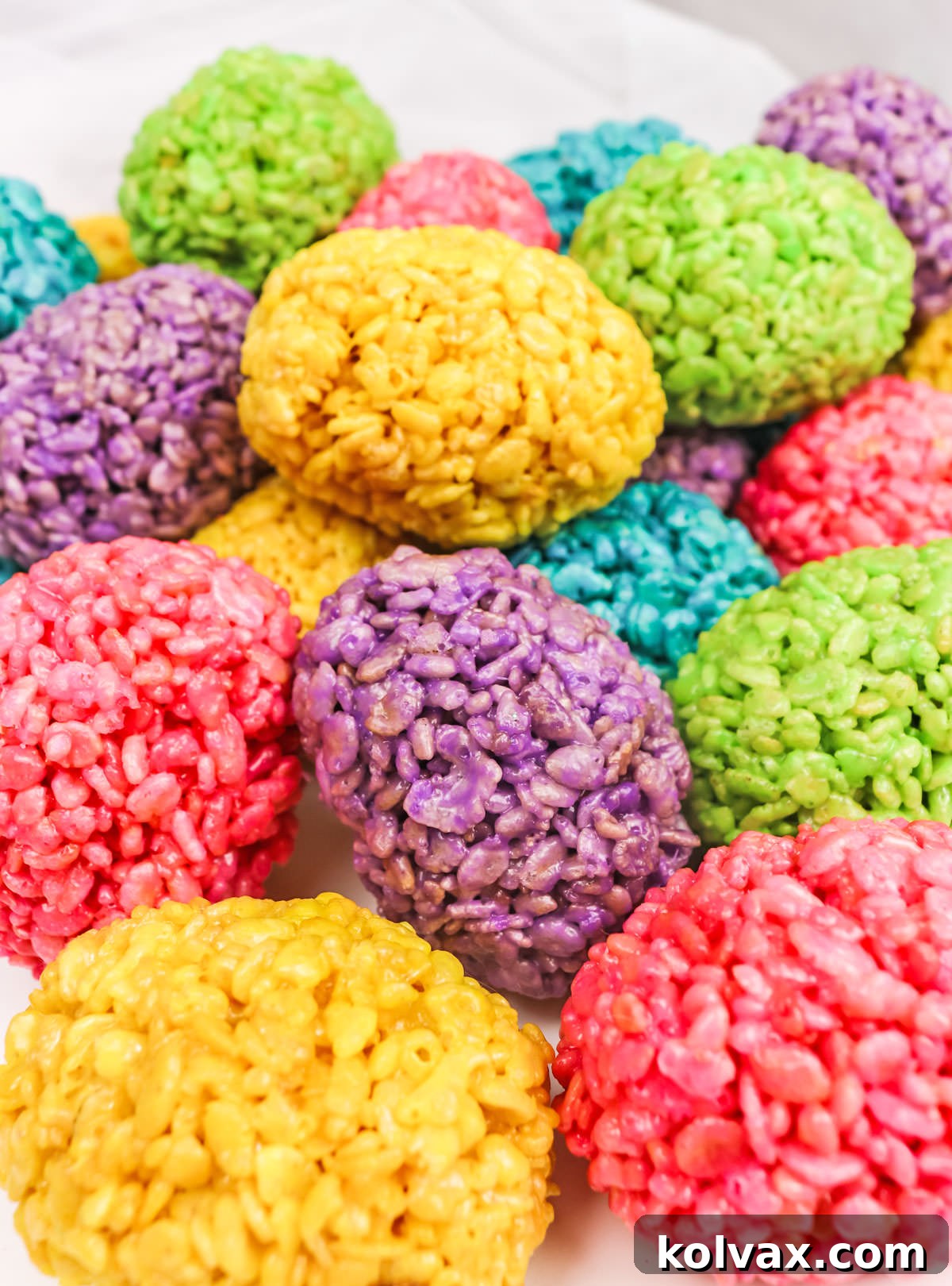 Closeup on a large, inviting pile of vibrantly colored Rice Krispie Easter Eggs resting on a clean white surface, showcasing their appeal.