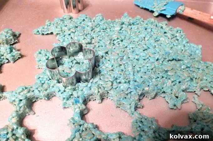 A small flower-shaped cookie cutter cutting out centers from blue Rice Krispie treats