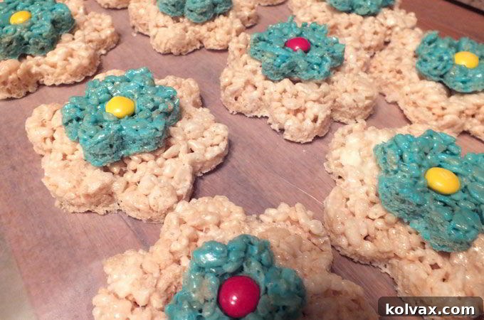 A red M&M being placed in the center of an assembled flower Rice Krispie treat